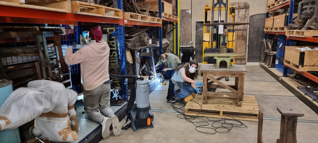 Ricardo Fonseca, Gabby Copeman and Sophie Hockaday cleaning objects on the roller racking with cleaning equipment and masks